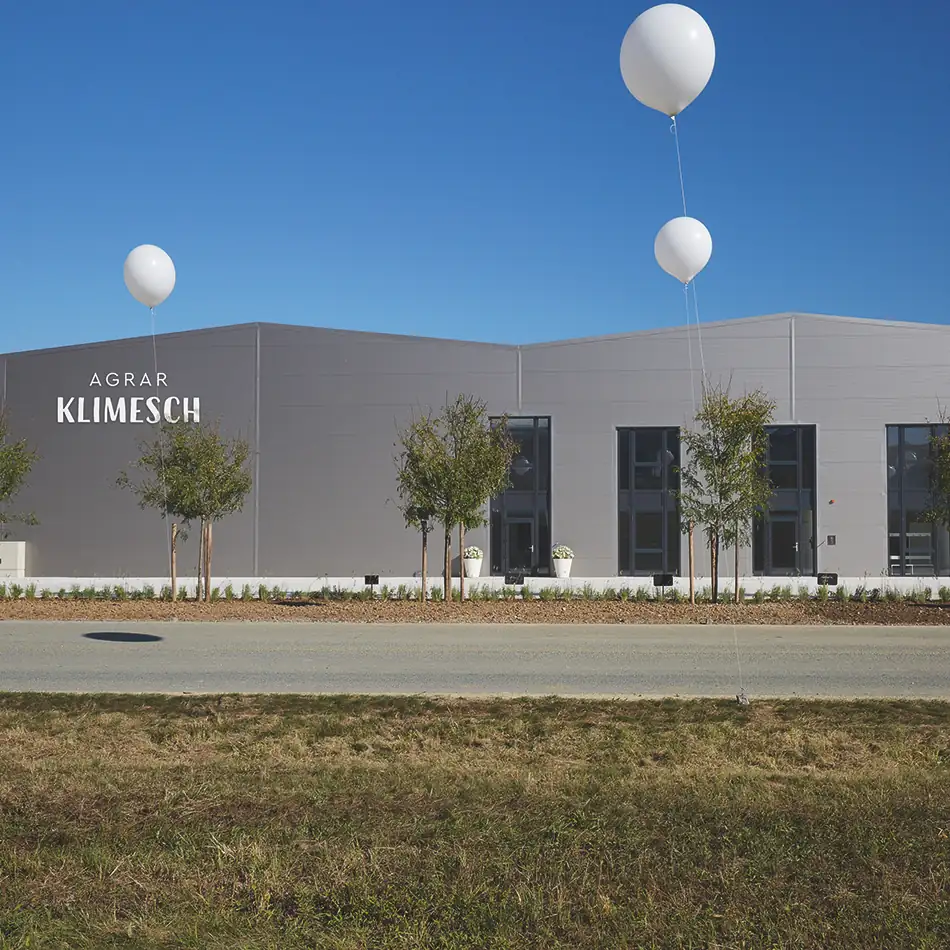 Das Betriebsgebäude von Agrar Klimesch: Modernes eingeschoßiges Gebäude, Fassade mit dunkelgrauen Platten verkleidet. 3 große weiße Luftballons zur Eröffnungsfeier.